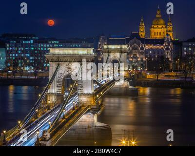 Budapest, Hungary - Blood Moon rising over downtown of Budapest with beautiful Szechenyi Chain Bridge and St. Stephen's Basilica by night Stock Photo