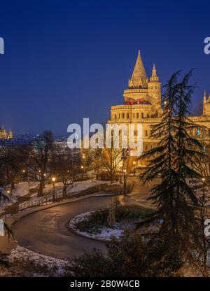 Budapest, Hungary - The north towers of the illuminated Fisherman's Bastion at blue hour with St. Stephen's Basilica and ferris wheel at background on Stock Photo