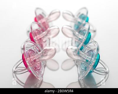 Boy and girl baby soothers in a row, pink and blue, facing off to illustrate gender inequality. Stock Photo