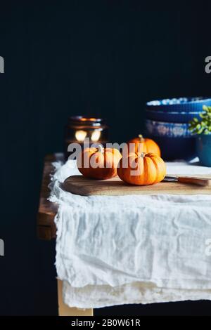 Still life with orange pumpkins on wooden table with white tablecloth and black background. Stock Photo