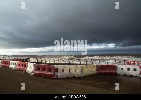 Red and white plastic safety barriers line the sea front as a storm approches. Stock Photo