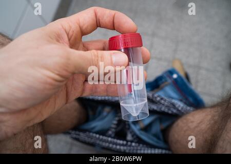 Stool Sample Container In Hands Of Man Sitting On Toilet Stock Photo