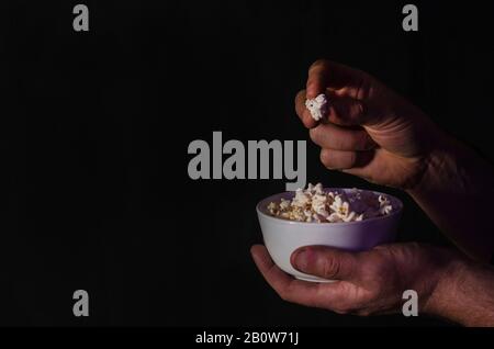 Popcorn in a cup in the hands of a man watching a movie on a black background with copy space. For articles about the movie. Cinema concept. Stock Photo