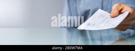 Close-up Of A Human Hand Giving Cheque On Desk Stock Photo