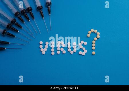 Tablets laid out with the word virus and syringes on a light blue background. Coronavirus spread. Viral infection. Medical concept. Stock Photo