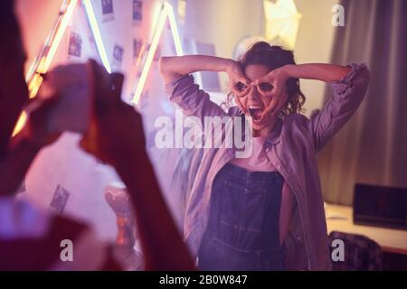 Young happy woman making a face and posing at camera while man photographing her at a party Stock Photo
