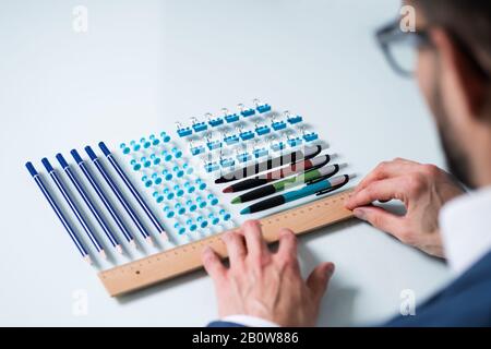 A Person's Hand Arranging Pencils And Multi Colored Pushpins In A Row On White Background Stock Photo