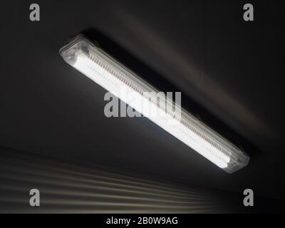 Close-up photo of a long luminous lamp hanging on dark ceiling Stock Photo