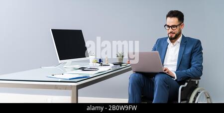 Full Length Of Young Handicapped Man Using Laptop While Sitting On Wheelchair At Home Stock Photo