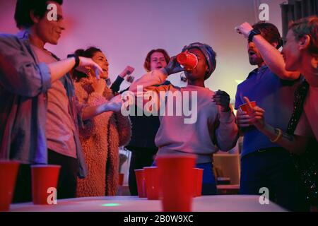 African young woman drinking beer while she playing together with her friends in beer pong during a party at home Stock Photo