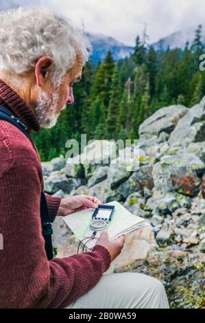 Mature Caucasian man using a map and compass in the mountains. Stock Photo