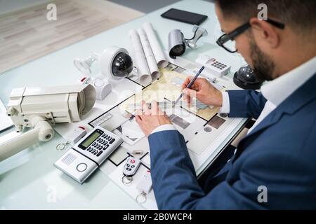 Architect Drawing Blueprint With Various Security Equipment On Desk Stock Photo