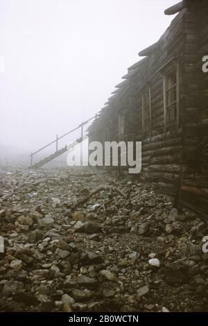 Abandoned ruins of the Mramorny camp of the Gulag forced-labour camp system in the Kodar Mountains in the Transbaikal Region in Siberia, Russia. The camp was established in January 1949 in the altitude about 2,150 metres (7,000 ft) above sea level to serve the nearby Uranium mine. The politician prisoners of Soviet regime used to work here in the extremely hard conditions. The wooden barrack pictured in the foreground was used as dwelling for camp guard while prisoners were forced to live in large canvas tents even in winter. The camp was closed in October 1951 because Uranium reserves were de Stock Photo