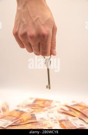 A man's hand holds a key over a pile of five-thousand-ruble bills.The concept of improving housing conditions. Stock Photo