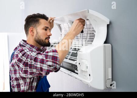 Happy Male Technician Repairing Air Conditioner With Screwdriver Stock Photo
