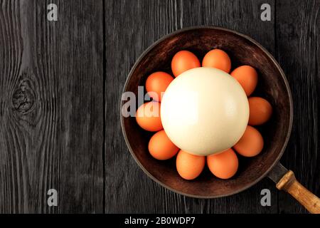Large ostrich egg surrounded by chicken eggs in an old cast-iron pan, close-up.