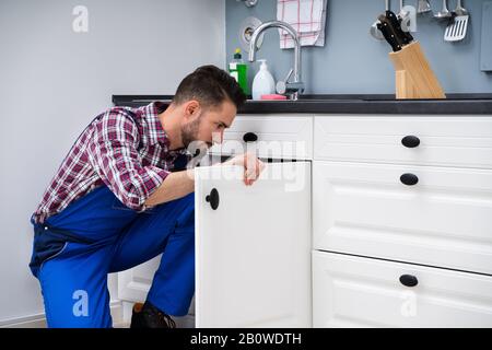 Young Handyman Fixing Sink Door In Kitchen Stock Photo