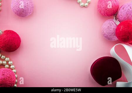Pink background with pink and red yarn or threads balls garland, white ribbon, jewelry box, pearl necklace. Lighting cotton thread balls. Valentines Stock Photo