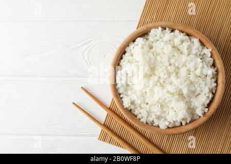 Bowl with boiled rice and chopsticks on wooden background, top view Stock Photo