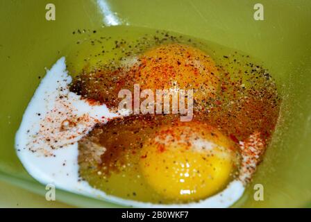 Close up of two raw seasoned eggs in a green plastic bowl Stock Photo
