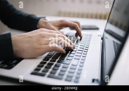 Male's hands typing on a laptop keyboard. Close-up view of man's hands typing over laptop black keyboard. Stock Photo