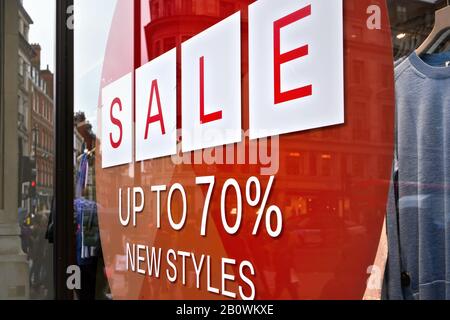 Sale up to seventy percent new styles sign - white letters in red circle - on glass window of clothes shop Stock Photo