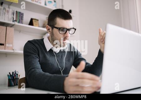 Businessman doing online meeting and video conference. Male employee takes part in online meeting while sitting in office and wearing headphones. Stock Photo