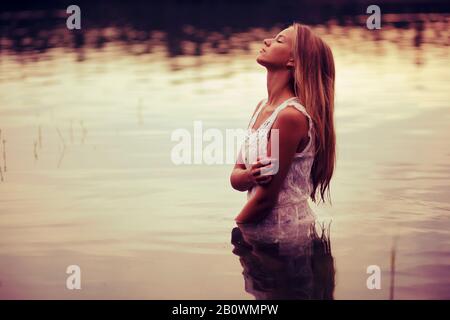Young woman in white dress stands in the water Stock Photo