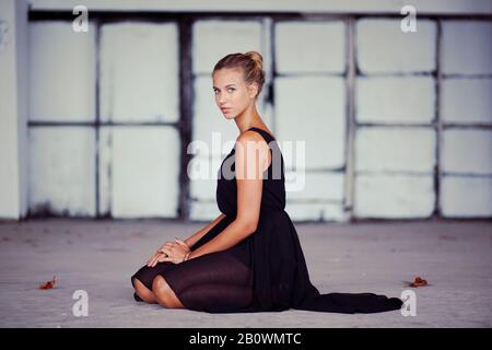 Young woman in black dress kneels on the floor Stock Photo