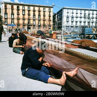 1960s, historical, Italian fisherman sitting mending their nets by Mergellina harbour, Naples, Campania, Italy, a fishing port in Chiaia at the foot of the Posillipo Hill. Stock Photo