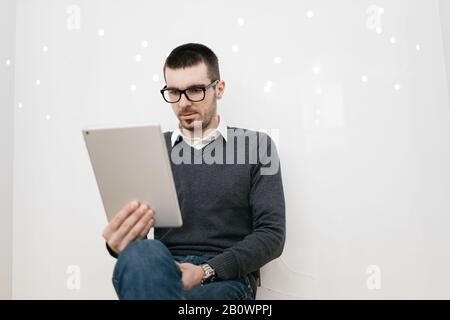 Serious man with glasses looking a tablet Bearded man wearing glasses sitting and using tablet while waiting in office. Stock Photo