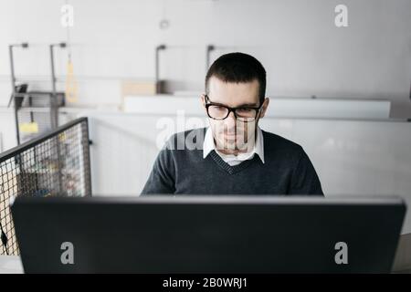 Serious guy looking into a computer desktop. Bearded male worker with glasses working on computer in office. Stock Photo