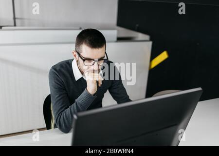 Focused worker searching online studies using computer. Employee with glasses working on computer in the working area. Stock Photo