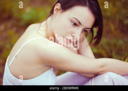Young woman sits thoughtfully on a meadow Stock Photo