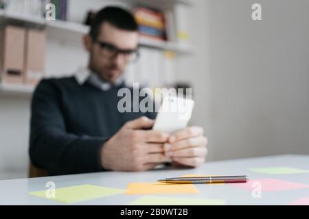 Elegant pen on table with sticky notes. Metal pen with colored sticky notes with blurred man holding on out of focus phone in office Stock Photo