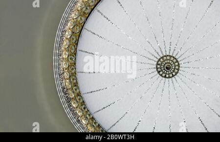 Round crystal chandelier with rays on the white plafond and a gilded fringing. Stock Photo