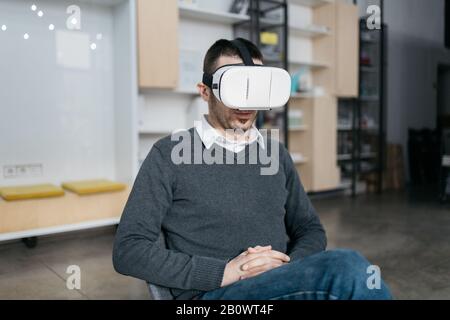 Man sitting and wearing a VR glasses. Entrepreneur testing virtual reality glasses while sitting in coworking space. Stock Photo