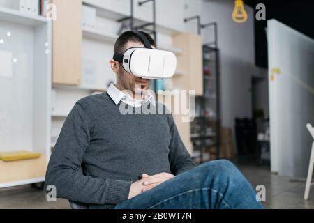 Entrepreneur testing virtual reality glasses while sitting. Young man sitting and wearing a VR glasses in the office. Stock Photo