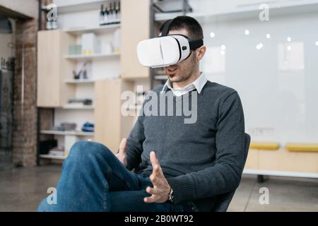 Businessman testing virtual reality headset for games. Bearded man wearing virtual reality headset and sitting in testing room. Stock Photo