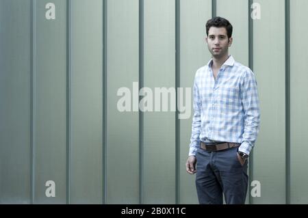 Young man in shirt stands in front of house wall, Stock Photo