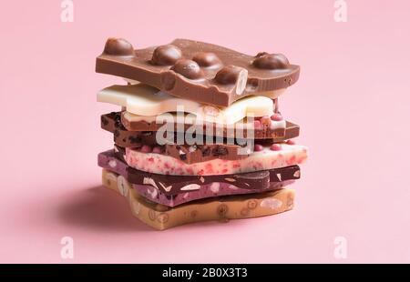 Assortment of fine Swiss chocolate. Mix of caramel, berries chocolate, white and dark chocolate in a stack, on pink background. Chocolate close-up. Stock Photo