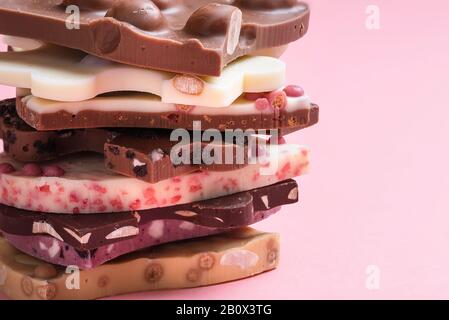 Swiss chocolate assortment in a stack on pink background. Mix of different types of chocolate. Chocolate close-up. Pieces of white and dark chocolate. Stock Photo