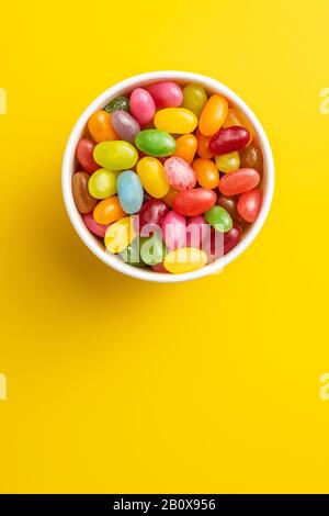 Fruity jellybeans. Tasty colorful jelly beans in bowl on yellow background. Top view. Stock Photo