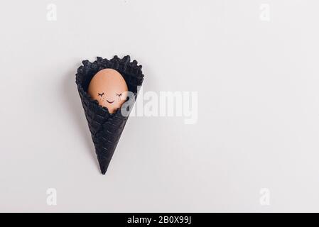 Easter eggs in black ice-cream horn on pastel beige background. Flat lay, Easter concept. Stock Photo