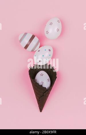 Easter eggs in black ice-cream horn on pastel pink background. Flat lay, Easter concept. Stock Photo