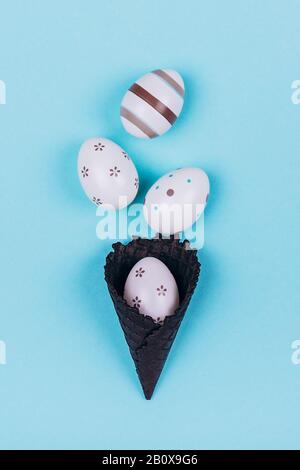 Easter eggs in black ice-cream horn on pastel blue background. Flat lay, Easter concept. Stock Photo