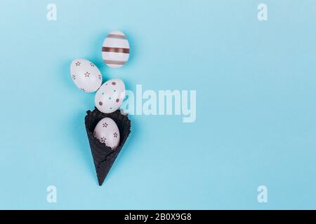 Easter eggs in black ice-cream horn on pastel blue background. Flat lay, Easter concept. Stock Photo