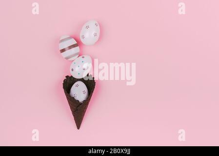 Easter eggs in black ice-cream horn on pastel pink background. Flat lay, Easter concept. Stock Photo