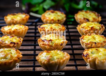 Filo pastry cups filled with feta mixture on a black cooling rack. Stock Photo