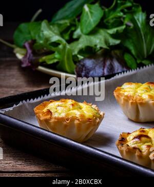 Filo pastry cups filled with feta cheese mixture, on a baking pan. Stock Photo